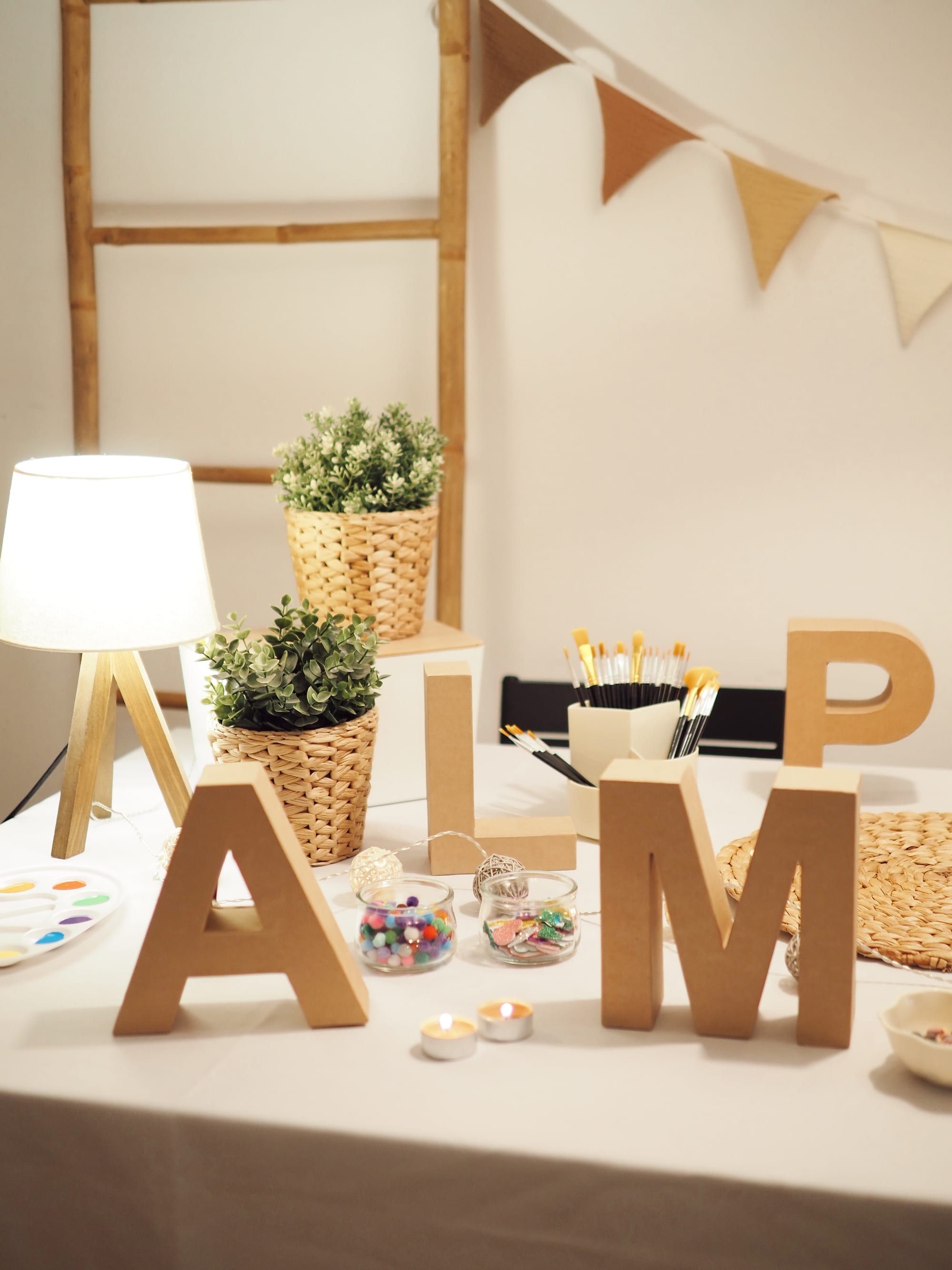 A corner set up with wooden letters, a lit lamp, plants and candles