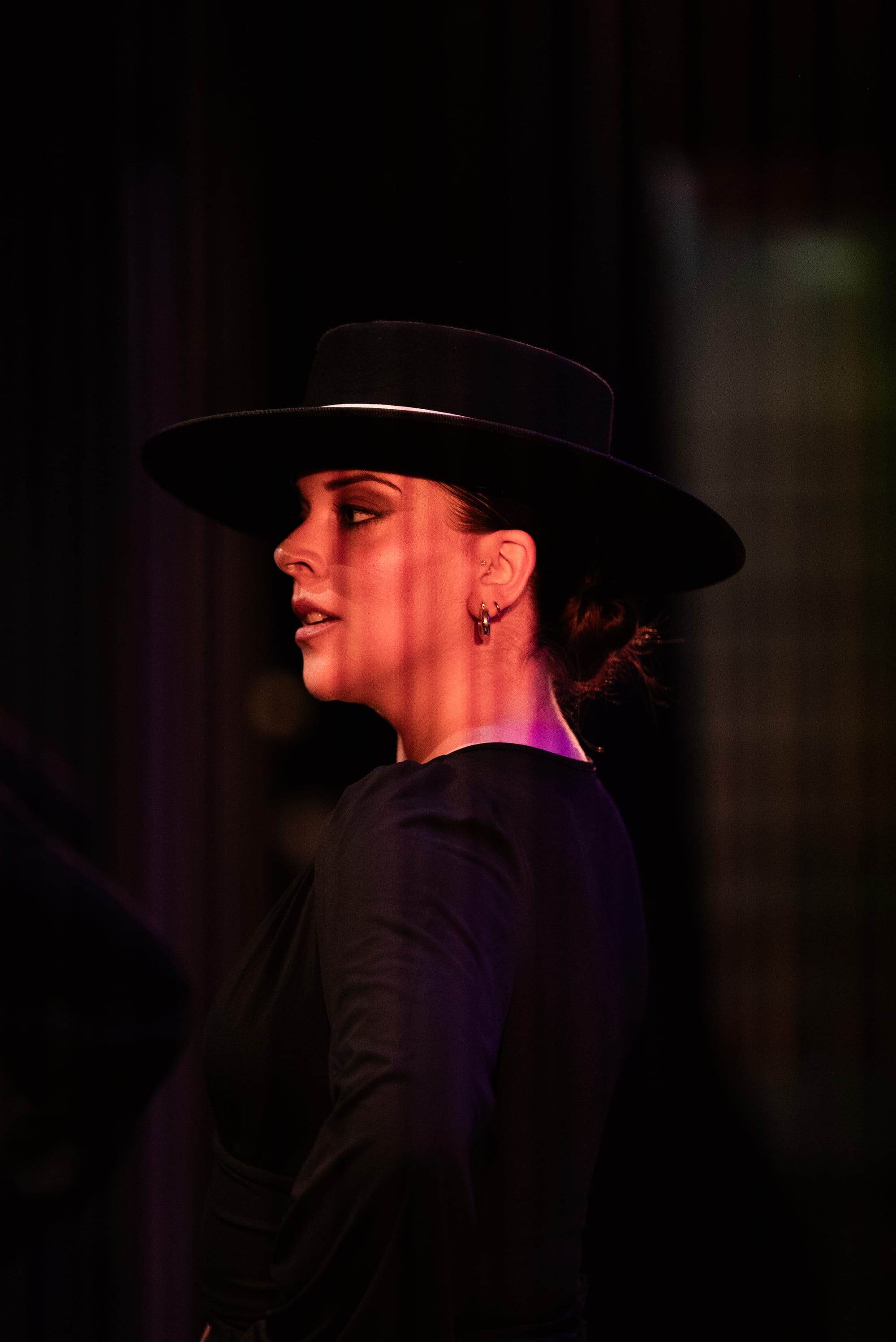Profile portrait of a dancer in a cordobés hat against a black stage