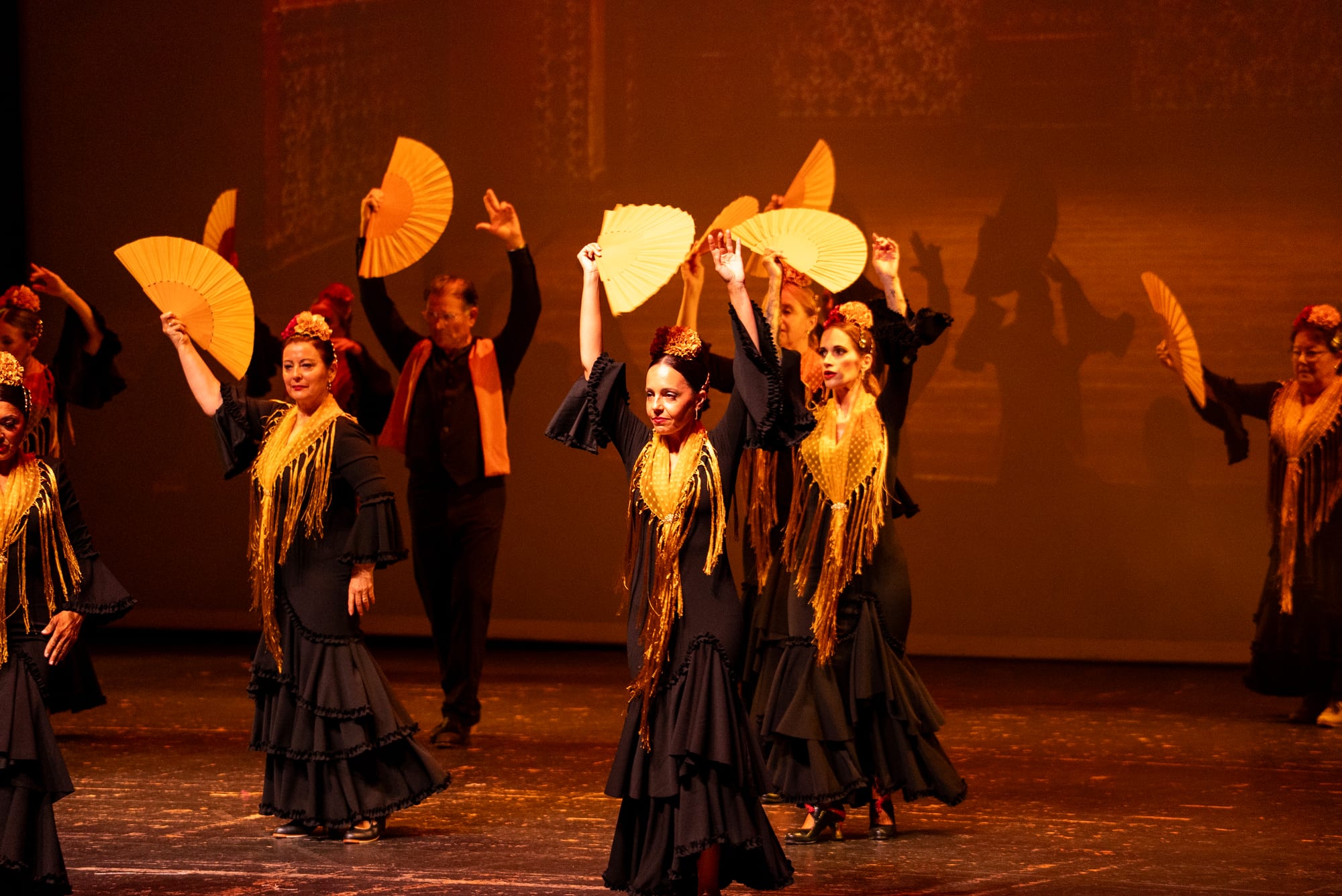 The company with yellow fans and black costumes under warm amber light