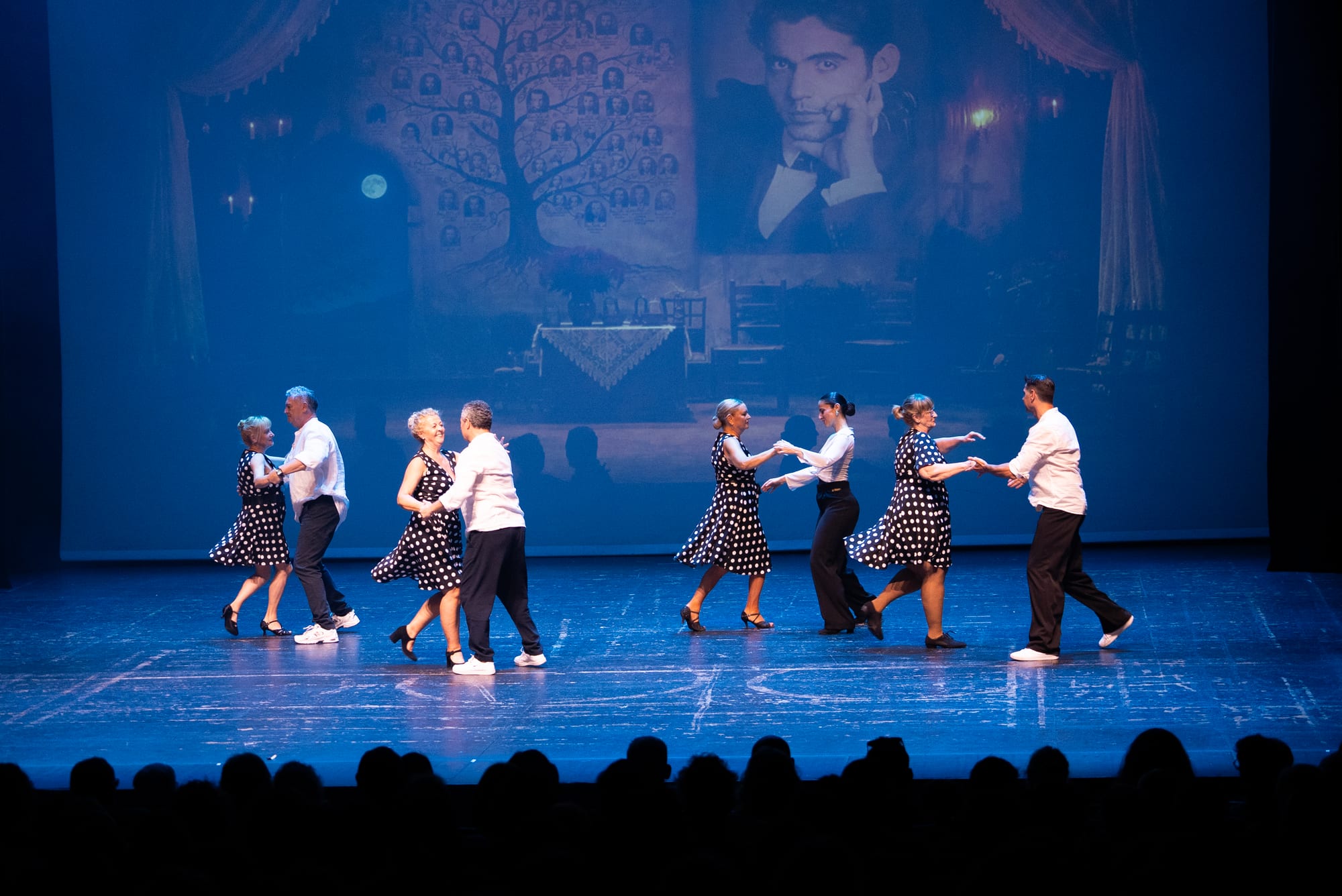 Couples dancing under blue light, a portrait of Lorca projected behind them