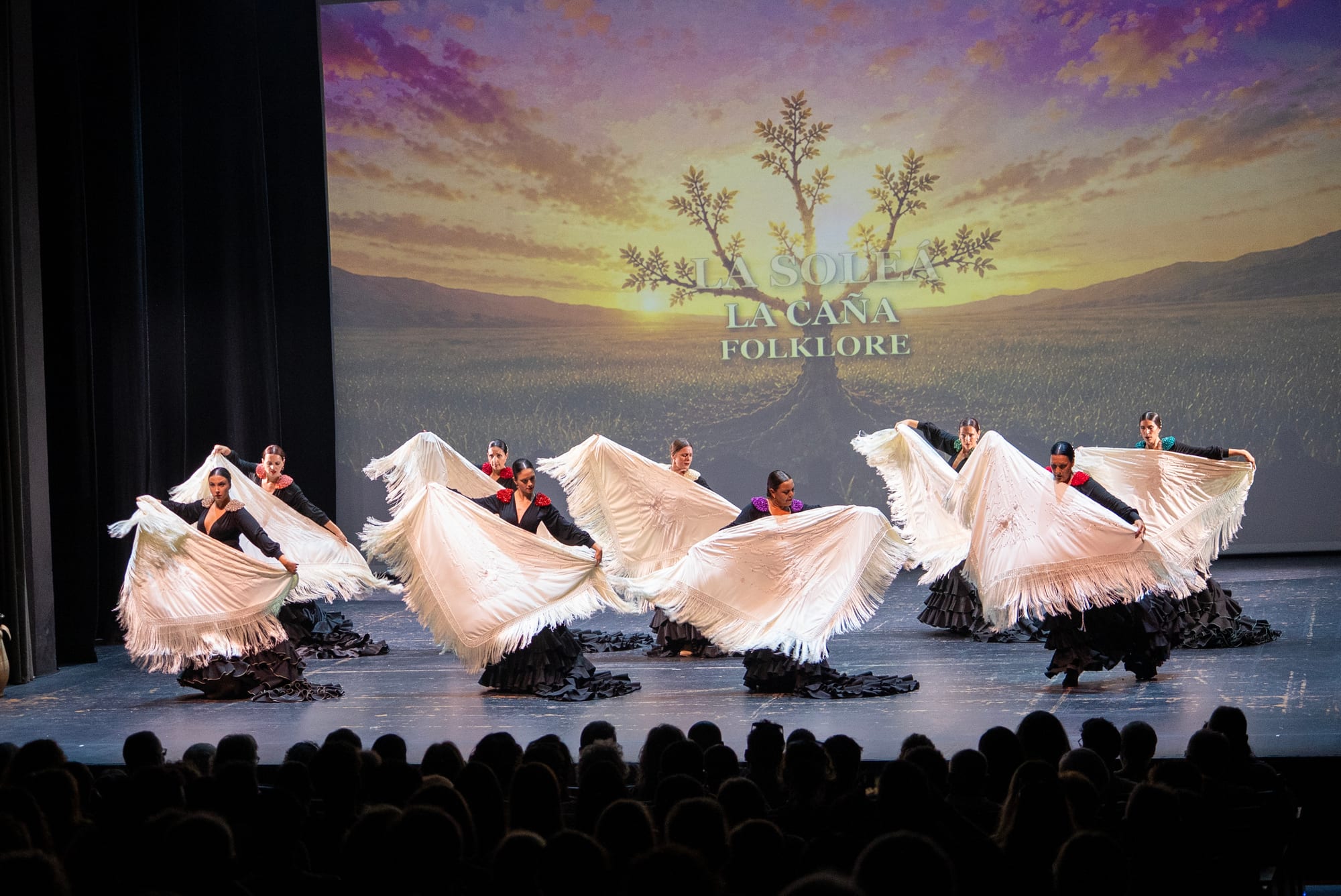 A line of dancers with white shawls against the La Soleá backdrop